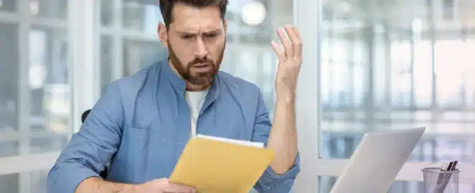 A stressed small business owner reviews messy financial documents at their desk.